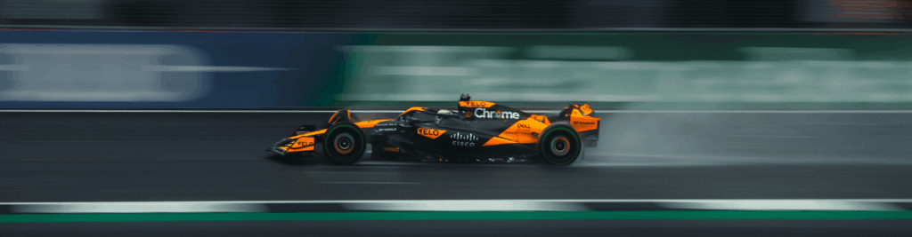 Orange and black McLaren Formula 1 car racing on a wet track at high speed, symbolizing fast-paced decision-making and performance-driven investment strategies.